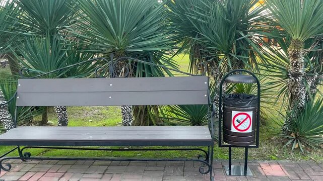 No Smoking Sign on a public trash can next to a rest bench