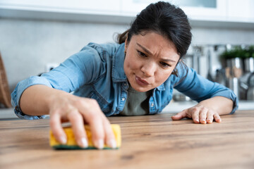 Obsessive compulsive disorder. Young woman with OCD rubbing kitchen top with sponge. Female...