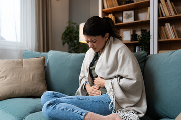 Stomach ache, cramps and hands of woman with abdomen pain due to constipation, menstruation or ibs issue. Sick, home and person suffering and holding belly in a house lounge, couch and living room