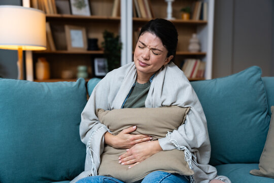 Stomach ache, cramps and hands of woman with abdomen pain due to constipation, menstruation or ibs issue. Sick, home and person suffering and holding belly in a house lounge, couch and living room