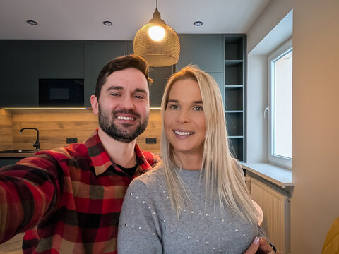 A young couple, a man and a woman of European appearance, take a selfie on a phone in a modern apartment.