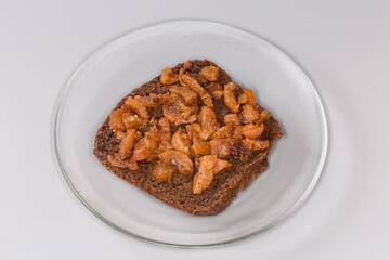 Open sandwich with duck сracklings and brown bread on saucer