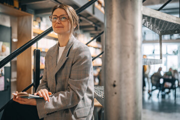 A woman in a plaid jacket sits on the stairs in a bookstore