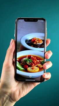 Medium shot, hands holding phone displaying the delicious food, holographic digital red hearts pop up from the phone screen against teal background.
