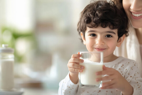 little boy holding glass of milk and his mother standing on background