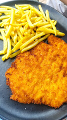 Delicious breaded schnitzel served with crispy golden fries on a dark plate, showcasing a classic...