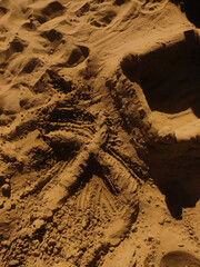 Intricate sand sculpture with visible footprints on bibione beach, italy, showcasing creative beach art under the warm july sun