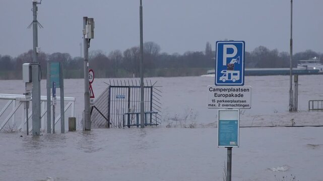 Cargo vessel sails on Rhine river, past flooded road and traffic sign in Tolkamer, an important measure station for water levels in the Netherlands