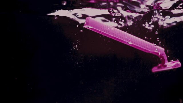 Pink razer falls and splashes in water against black backdrop.