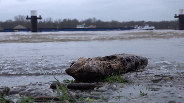 Low angle view of flooded road and quay in Tolkamer, with cargo vessels and ships in the background. High water levels of the Rhine river and heavy rainfall in Europe.
