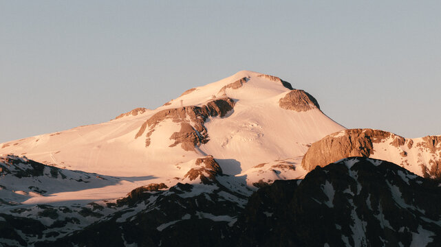 Vue  a&eacute;rienne d'un sommet montagneux, partiellement recouvert de neige, illumin&eacute; par la chaude lumi&egrave;re dor&eacute;e du soleil levant. Paysages alpins vus par drone. 