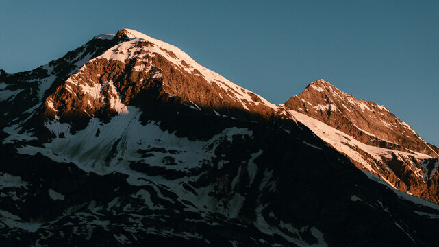 Vue  a&eacute;rienne d'un sommet montagneux, partiellement recouvert de neige, illumin&eacute; par la chaude lumi&egrave;re dor&eacute;e du soleil levant. Paysages alpins vus par drone. 