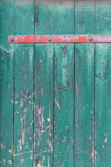 Wooden door made of old wooden planks in turquoise color with a red metal strip on top, the textured surface emphasizes the vintage charm and character.