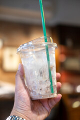 Close up of hand holding iced coffee plastic cup with a little ice with blurred background
