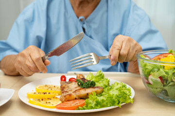 Asian elderly woman patient eating salmon stake and vegetable salad for healthy food in hospital.