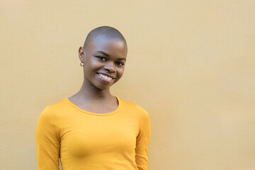 Obraz premium Smiling African woman with a shaved head in a vibrant yellow sweater