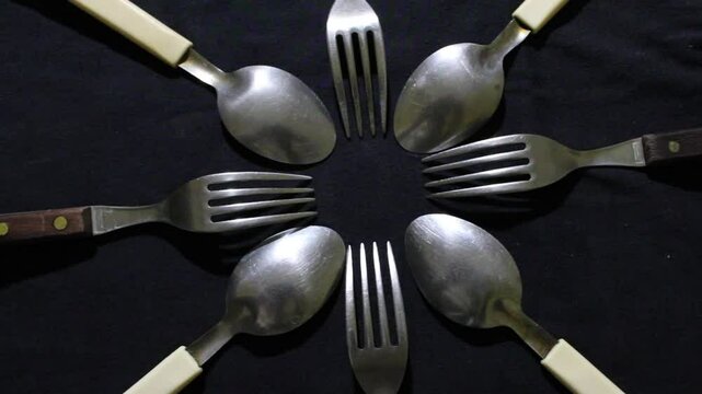 Cucharas y tenedores grandes en c&iacute;rculo, son herramientas culinarias para diversos alimentos, forman un dise&ntilde;o de brillos y texturas abstractas con fondo negro.