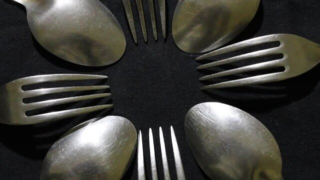 Cucharas y tenedores grandes en c&iacute;rculo, son herramientas culinarias para diversos alimentos, forman un dise&ntilde;o de brillos y texturas abstractas con fondo negro.