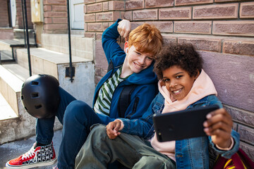 Two boy kids using smartphones and laughing outside school with skateboard