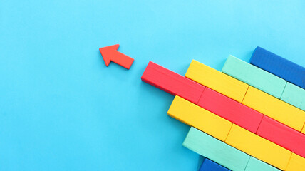 Wooden colorful cubes and red arrow on blue background. Concept of leadership and moving ahead