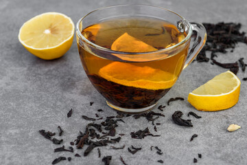 Glass cup of black tea with lemon on gray background.