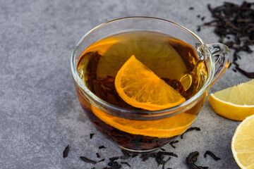 Glass cup of black tea with lemon on gray background.
