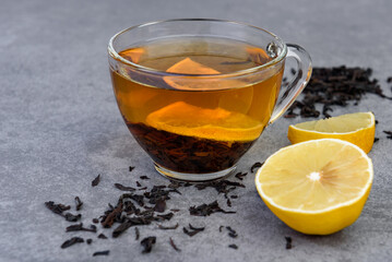 Glass cup of black tea with lemon on gray background.