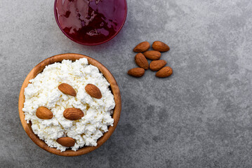 Cottage cheese in wooden bowl with almond and strawberry jam on gray background.