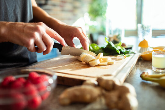 Close up woman hands cutting fresh ingredients for smoothie on a wooden board