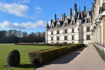 Fototapeta premium Majestic French Castle Surrounded by Lush Green Landscape and Blue Sky