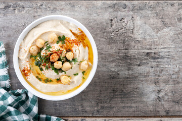 Chickpea hummus with olive oil, parsley and paprika in bowl on wooden table. Top view. Copy space