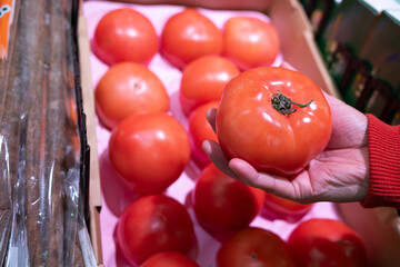 Hand grabs a tomato from the supermarket shelf