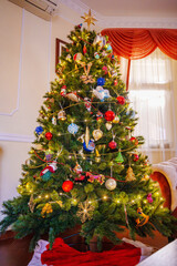 A large decorated artificial Christmas tree in the home interior. New Year's family traditions.