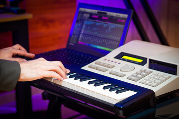 male professional music producer, composer, arranger hands playing on midi keyboard keys with music sequencer in home studio. music production