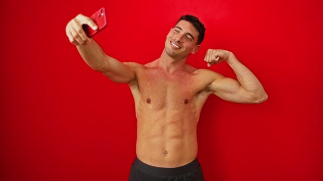 Young man taking a selfie flexing muscles against a bright red wall captures a playful and confident moment.