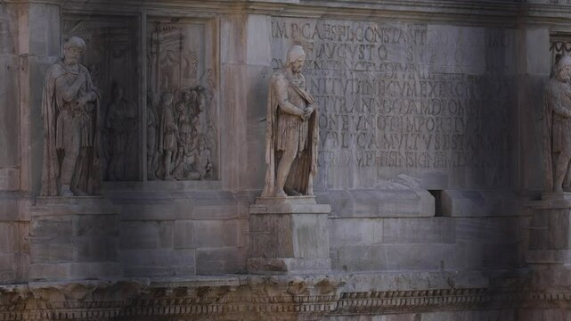 A statue of a man holding a shield is on a wall. The statue is surrounded by other statues and the wall is made of stone