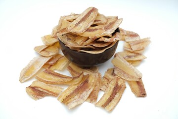 Crispy banana chips in a black bowl with scattered pieces around, against white background, showcasing a delicious and healthy snack.