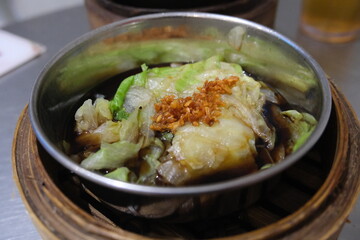 Steamed lettuce with soy sauce and crispy garlic, served in a metal bowl on a bamboo steamer, showcasing a delicious Asian dish.