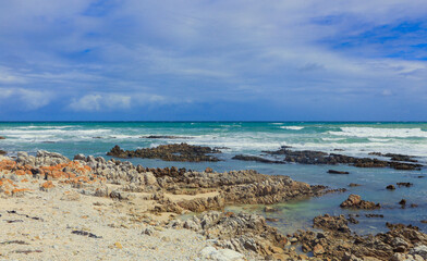 Coastal view of South African rocky shoreline with azure waves and cloudy sky at midday
