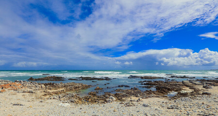Vibrant ocean and rocky shore of South Africa under bright clouds