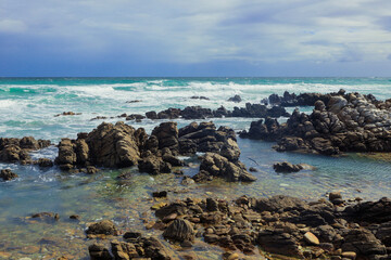 Obraz premium Coastal rocks and waves create a tranquil view along the South African shoreline at midday
