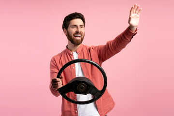 Happy man holding steering wheel, waving by hand, isolated on pink background