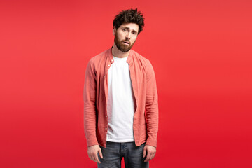 Disgruntled sleepy young man with grim smile standing over red background