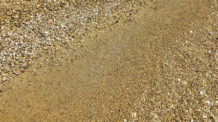 A background of sand and pebbles with natural relief patterns created by the wind. Golden sea sand texture, coarse-grained surface.