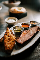 Delicious barbecue platter with smoked brisket, grilled bread, and dipping sauces served in a rustic restaurant