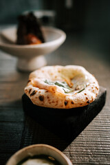 Freshly baked naan garnished with herbs served on a rustic wooden table in a cozy restaurant setting