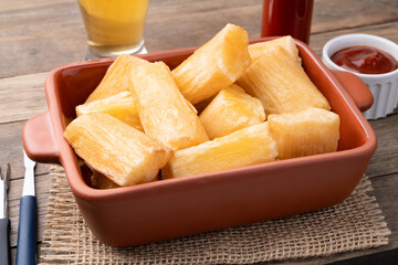 Traditional brazilian fried manioc in a plate with ketchup, pepper and beer over wooden table