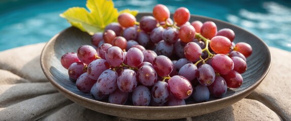 Fresh red grapes served in a bowl beside a tranquil pool, highlighting relaxation and summer vibes. Perfect for food and lifestyle imagery.