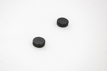 Two old black ice hockey pucks laying on ice.