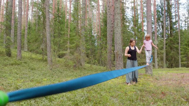 Teenage girl helping a her sister balance on a slackline in the forest